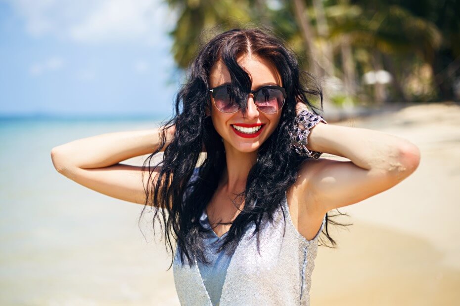 Mujer en la playa sujetándose en cabello y sonriendo, sobre los 6 pasos para obtener unas ondas playeras perfectas