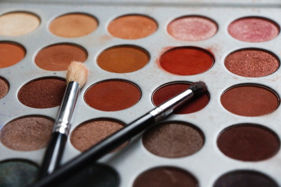 Paleta de sombras con tonos cálidos rojizos junto a brochas para ojos